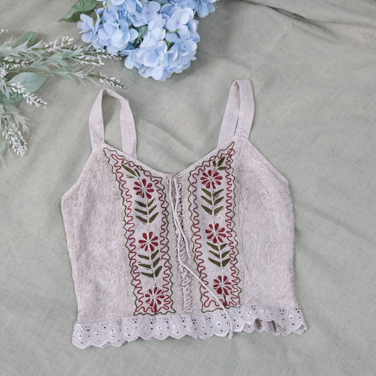 Embroidered crop top with floral patterns on a gray surface with flowers.