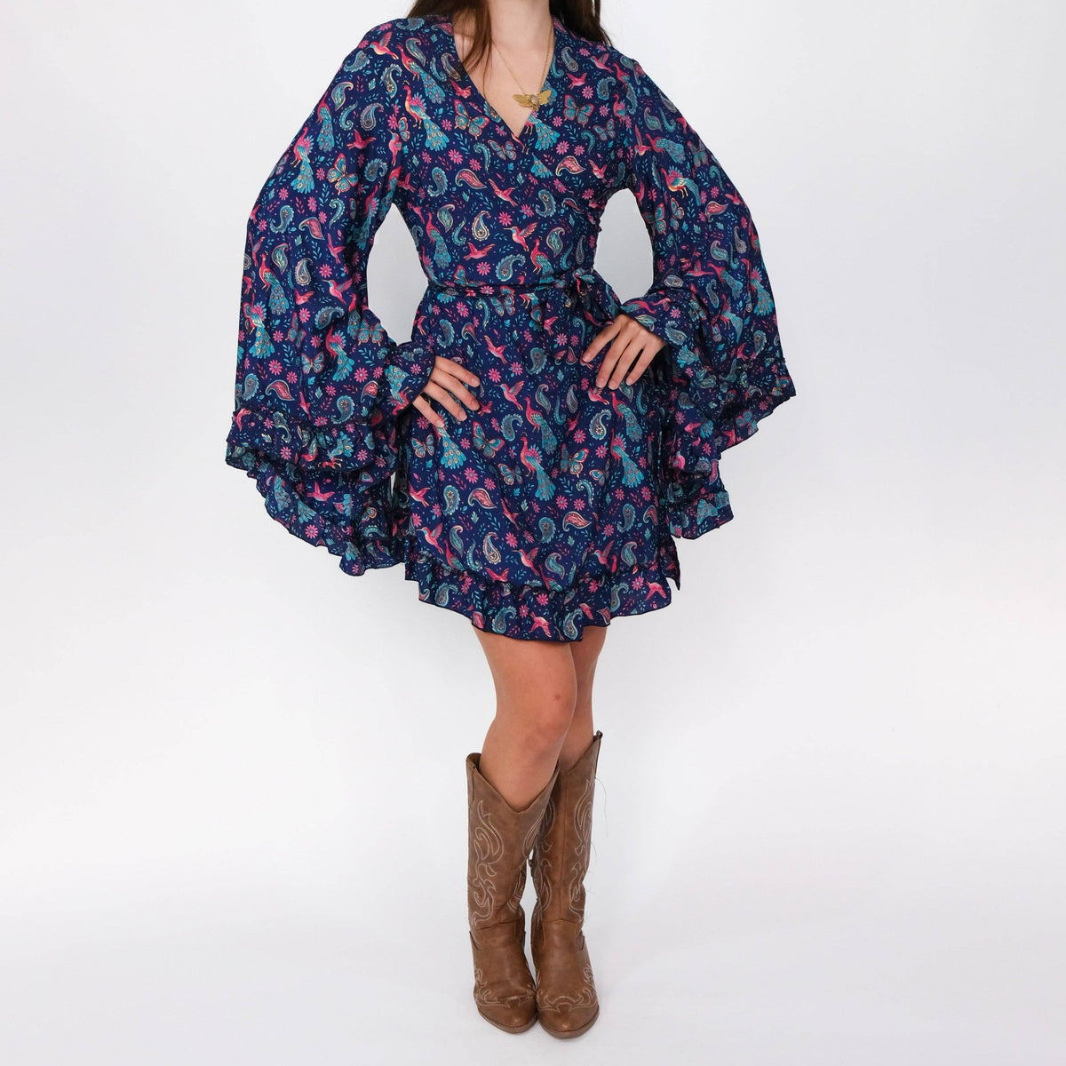 Person wearing a floral dress with bell sleeves and brown boots on a white background
