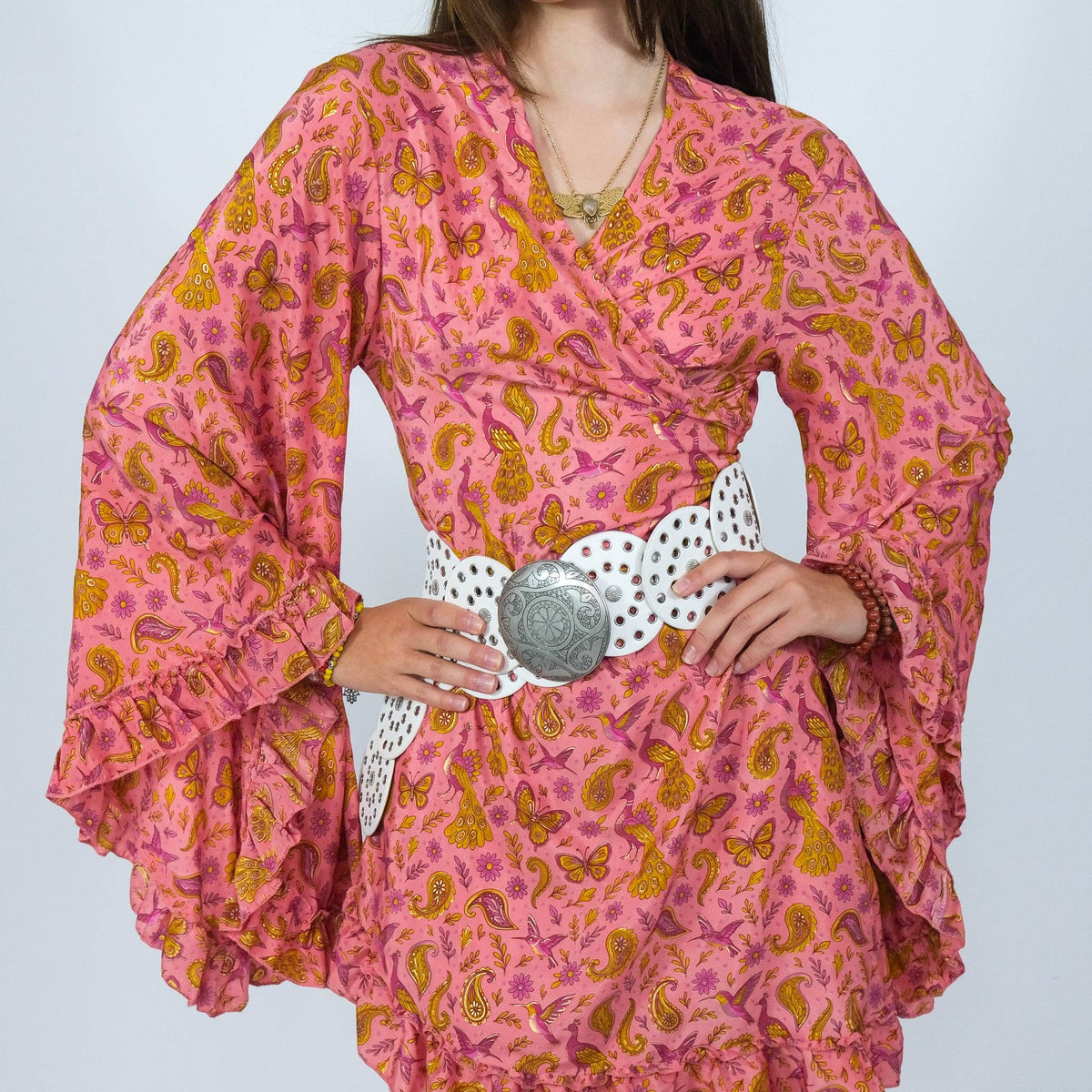 Person wearing a pink dress with yellow patterns and a white belt on a light gray background
