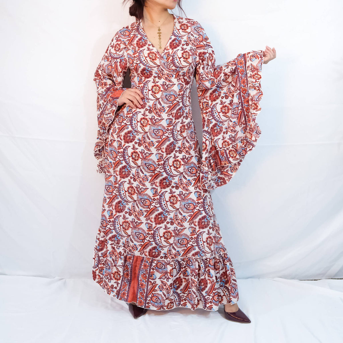 Person wearing a long, patterned dress with bell sleeves on a white background
