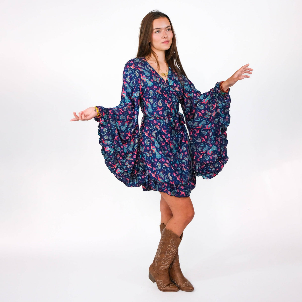Woman wearing a floral dress with wide sleeves and brown boots on a white background