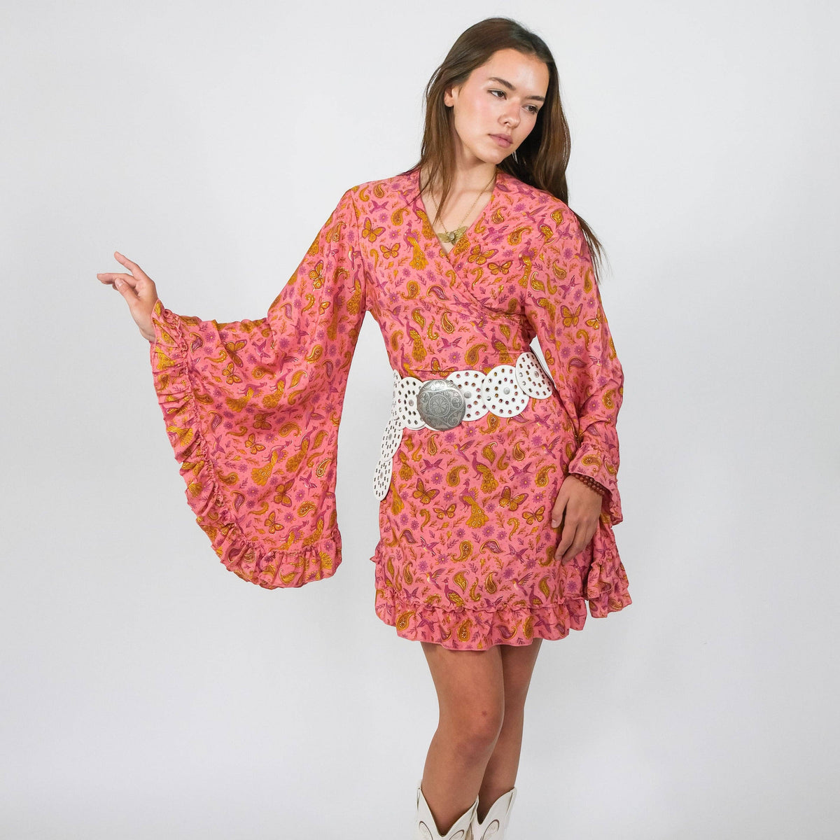 Woman wearing a pink floral dress with long sleeves and a white belt against a plain background