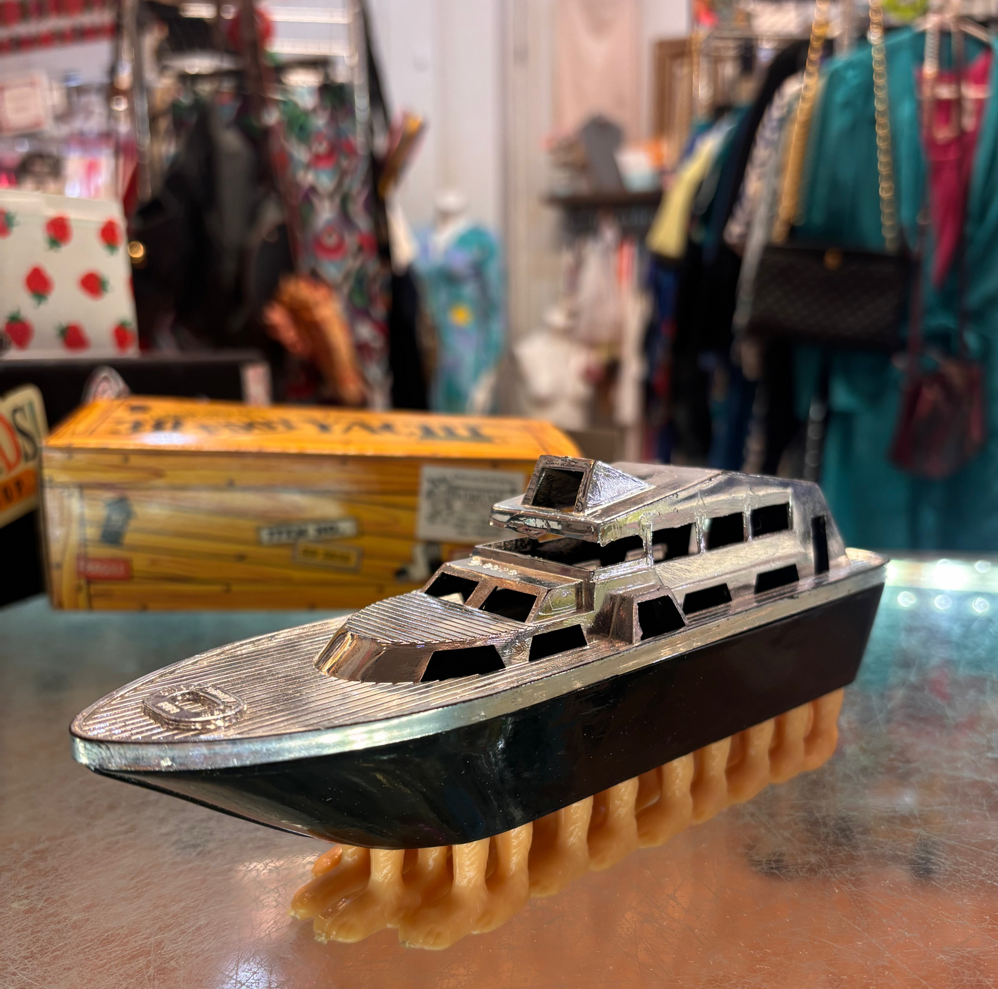 Toy boat with a brush on a reflective surface, with a store setting in the background.