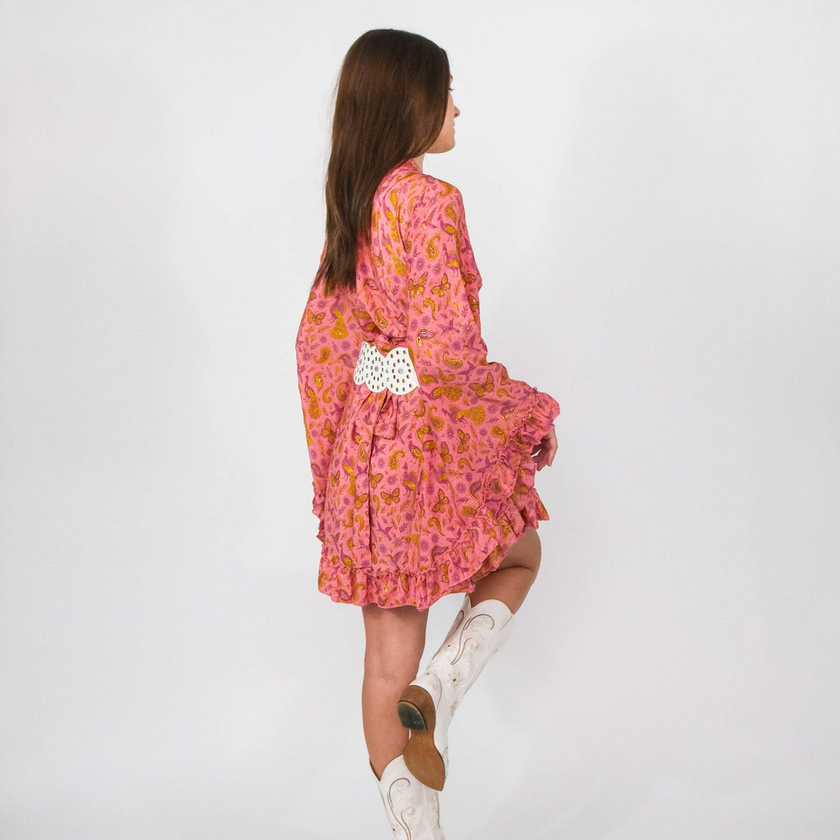 Woman wearing a pink floral dress with white boots on a plain background