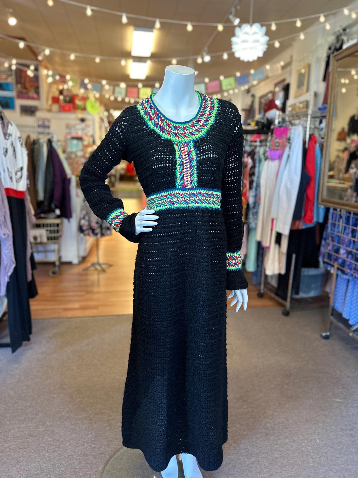 A black hand crocheted rainbow dress with small sleeves, displayed on a mannequin in a retail setting.