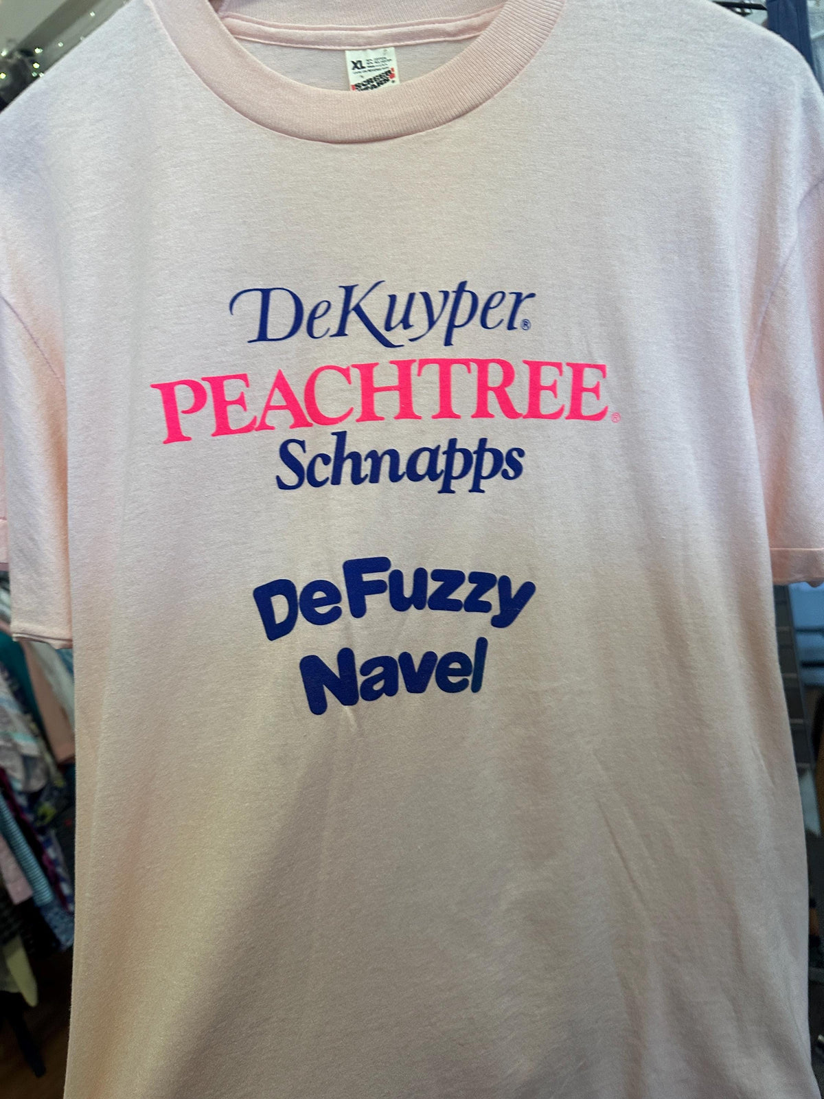 White t-shirt with colorful text 'DeKuyper Peachtree Schnapps DeFuzzy Navel' on a plain background.