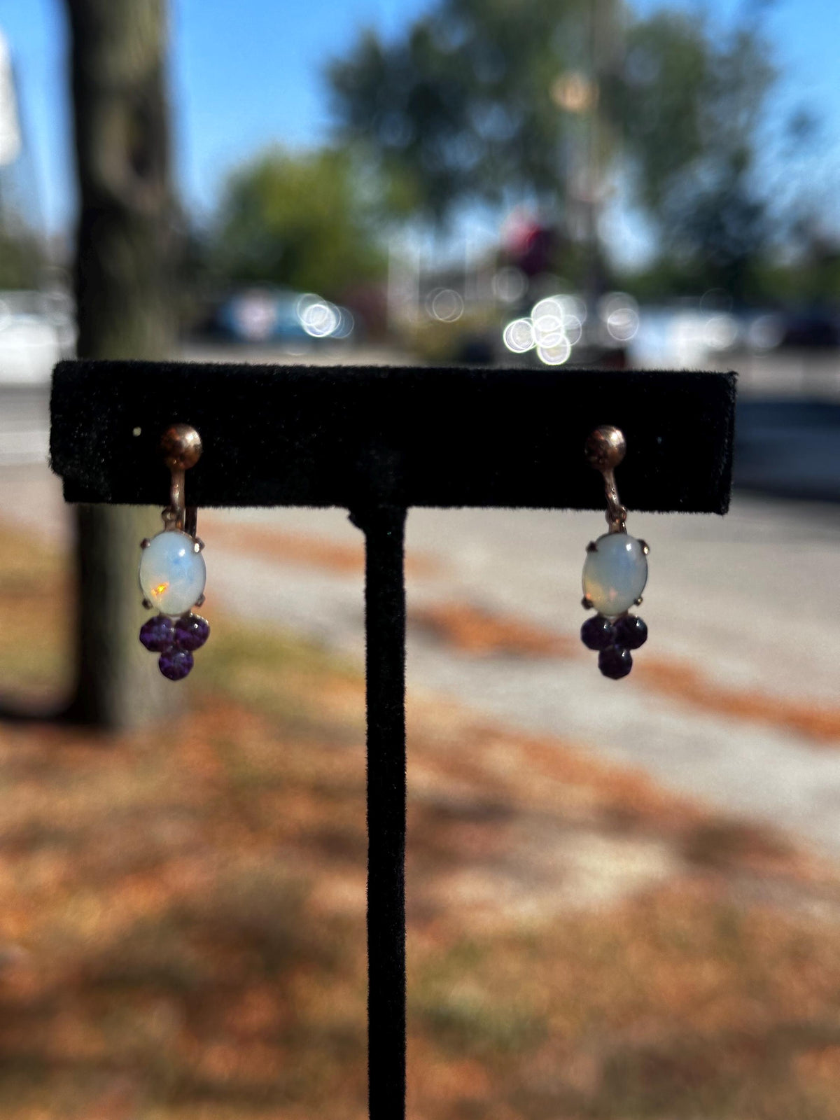Pair of earrings on a black stand with a blurred outdoor background