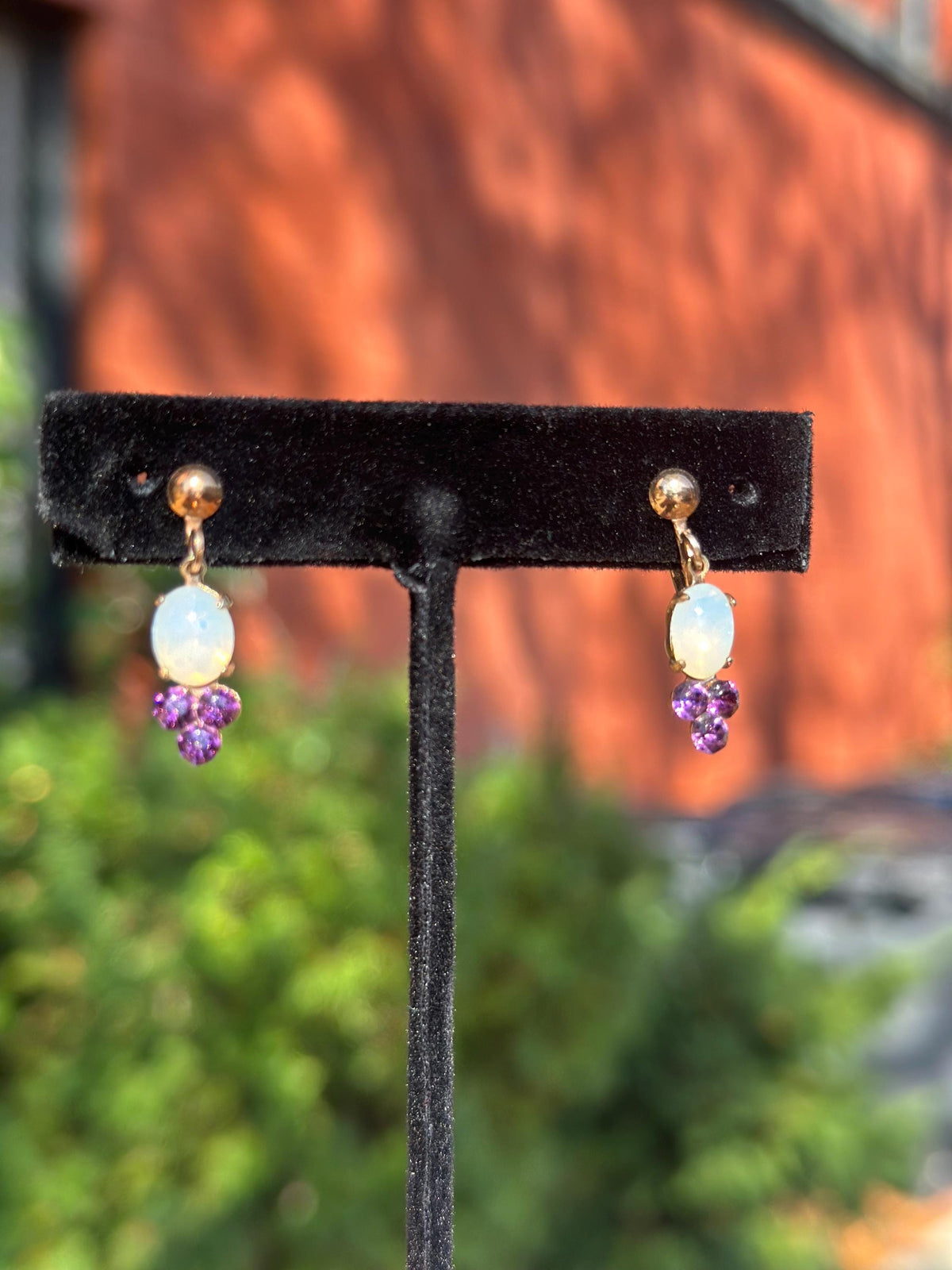 Pair of earrings with opal and purple gemstones on a black stand against a blurred background