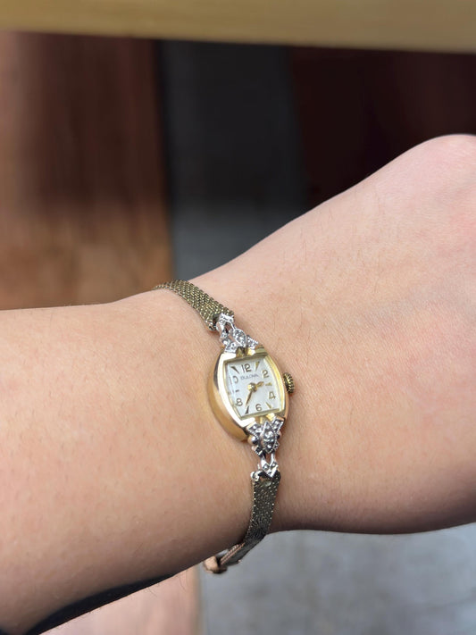 Gold watch with diamond accents on a wrist against a blurred background