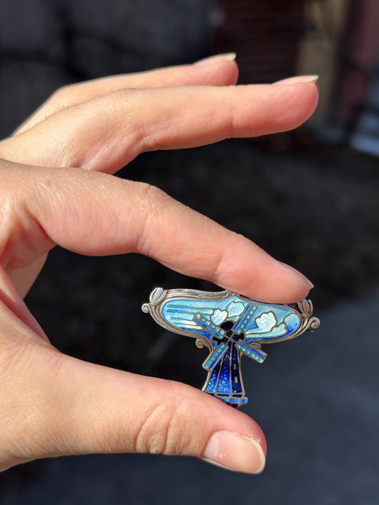 Hand holding a decorative brooch with intricate design against a blurred background