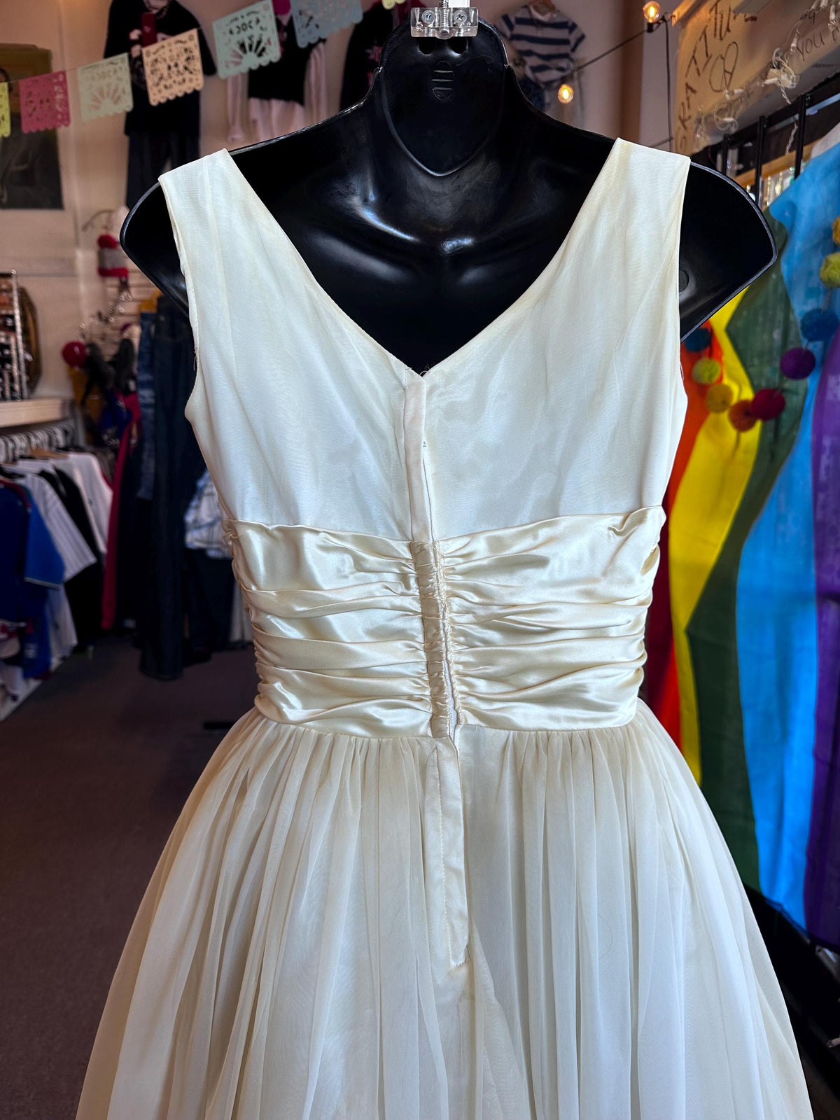 White dress on a mannequin in a store setting with colorful clothes in the background