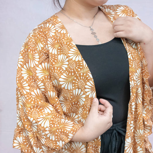 Person wearing a patterned orange and white kimono-style garment over a black top against a plain background