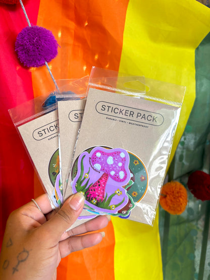 A hand holds three packaged sticker packs labeled 'STICKER PACK' against a bright rainbow-colored background with pom-poms. The front sticker shows a colorful mushroom illustration.