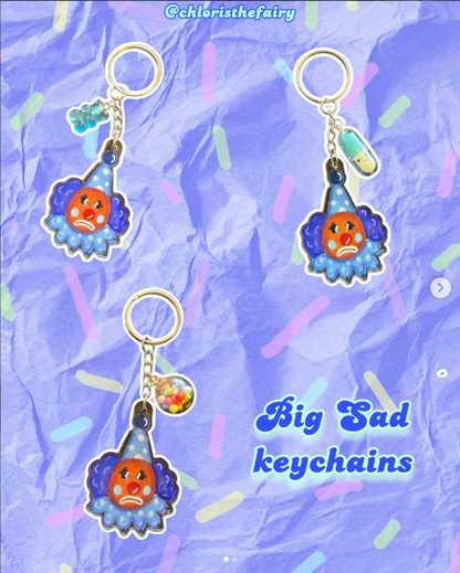 Three colorful keychains with sad face designs on a blue textured background.