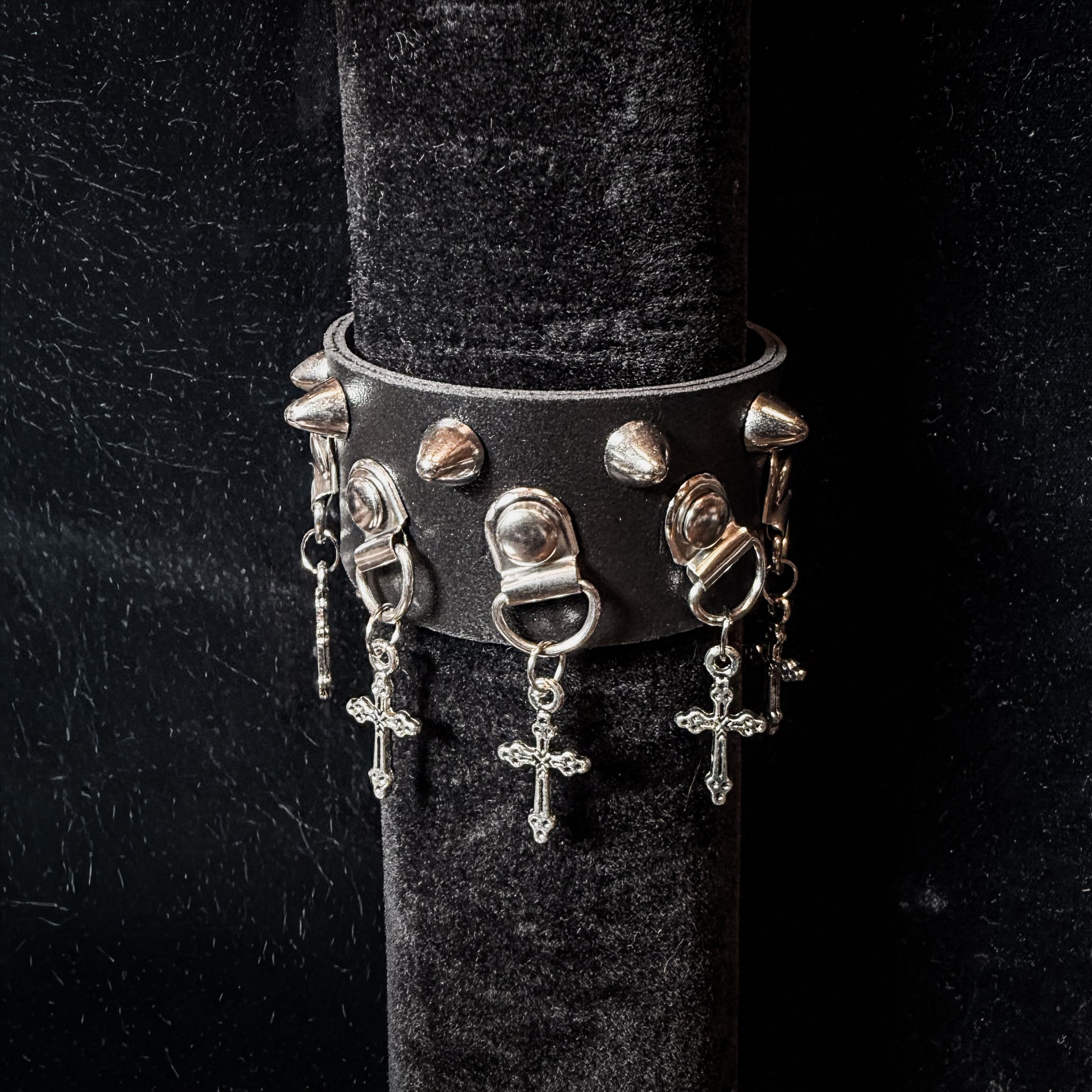 Black leather bracelet with silver spikes and charms on a black stand.