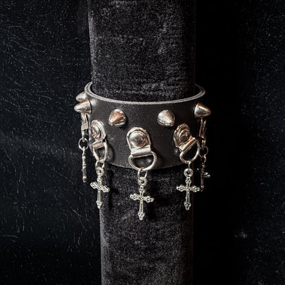 Black leather bracelet with silver spikes and charms on a black stand.