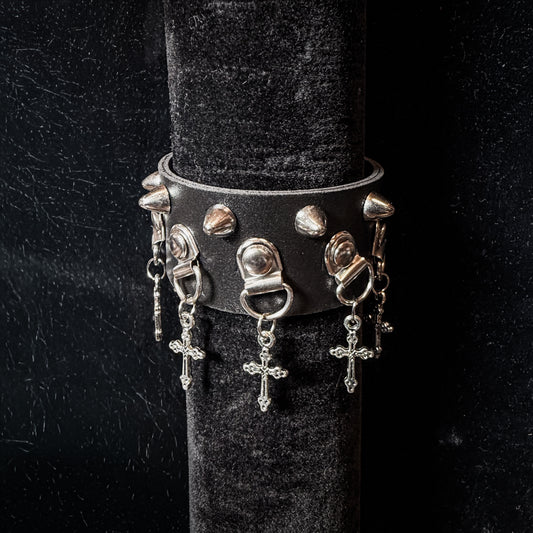 Black leather bracelet with silver spikes and charms on a black stand.
