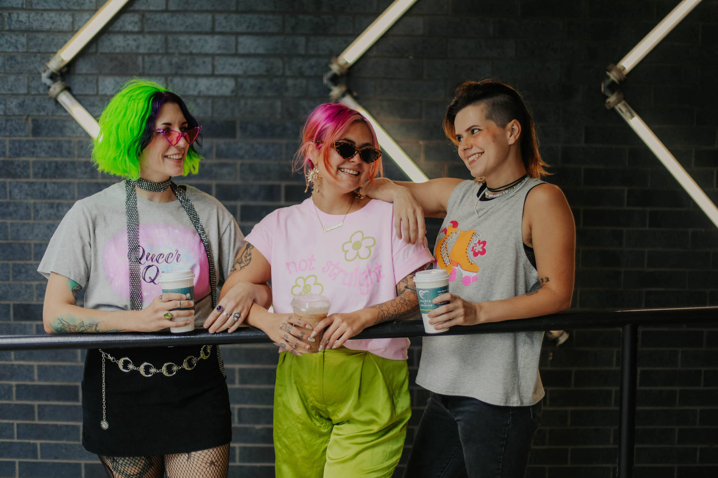 Three people with colorful hairstyles and clothing standing together against a dark brick wall.