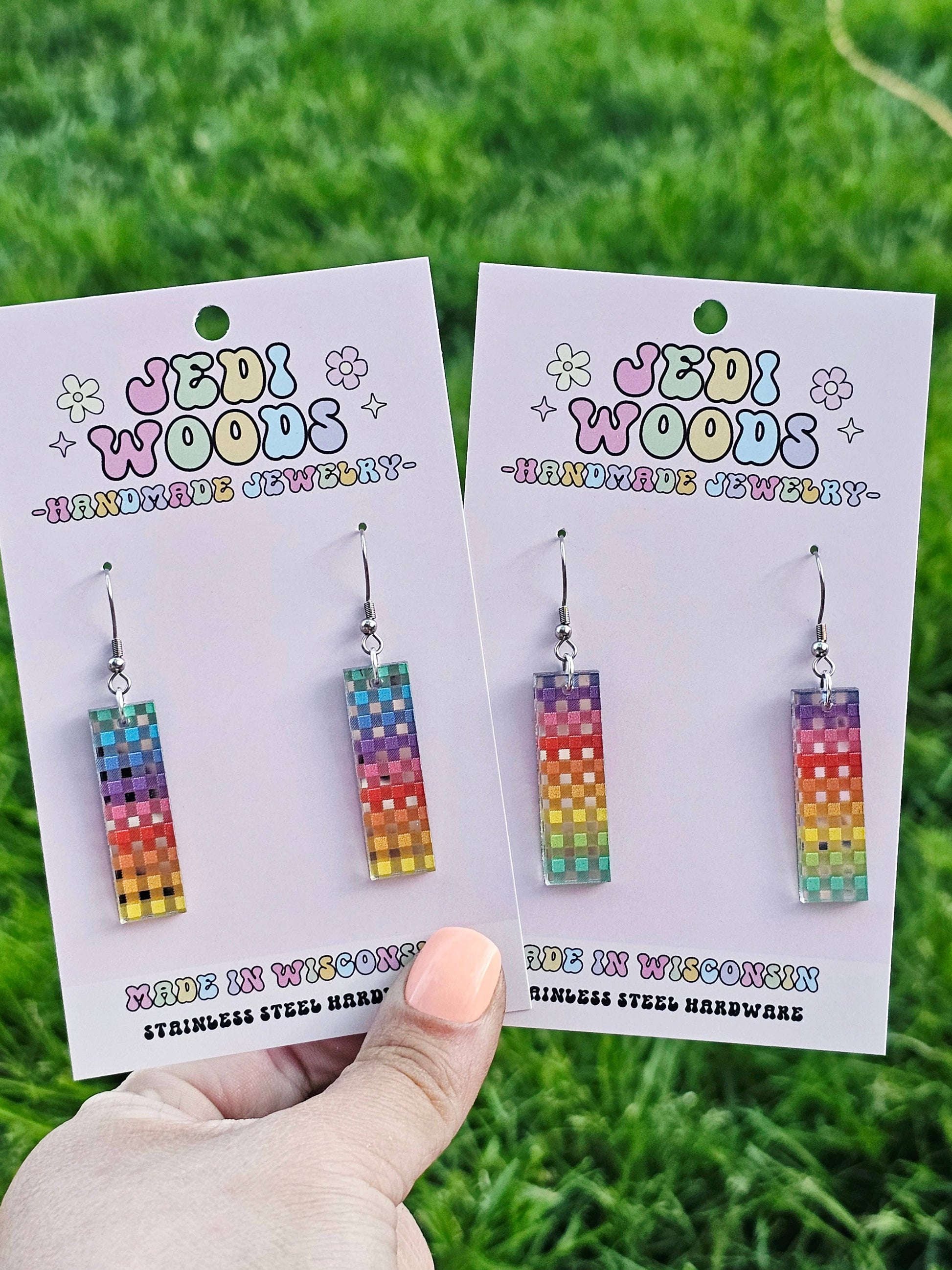 Colorful earrings on 'Jedi Woods' branded cards held against a grass background