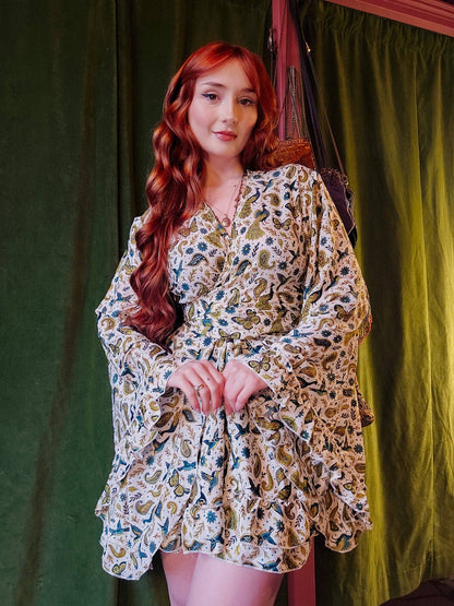 Woman wearing a floral dress standing against a green curtain.