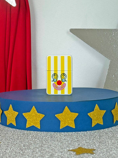 Card with a clown face design on a blue platform with gold stars, against a red curtain background.