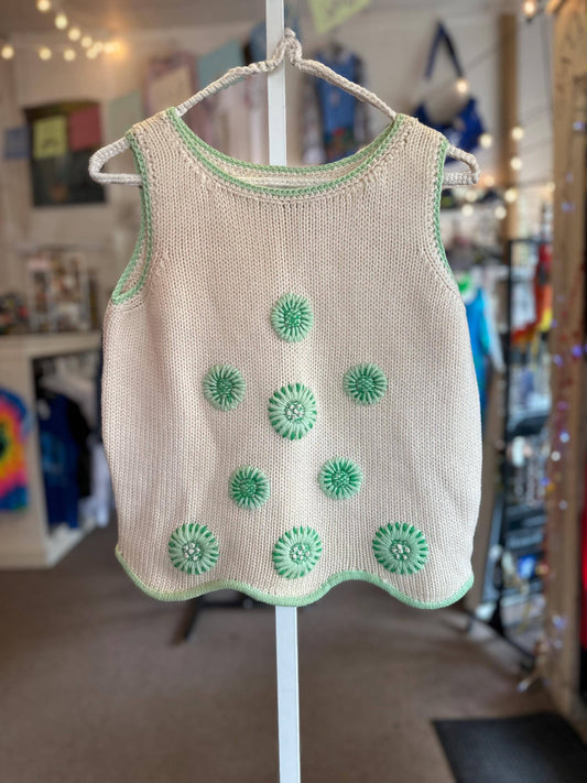 Beige knitted tank top with green floral patterns on a hanger in a store setting.