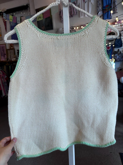 Knitted sleeveless top with green trim on a hanger