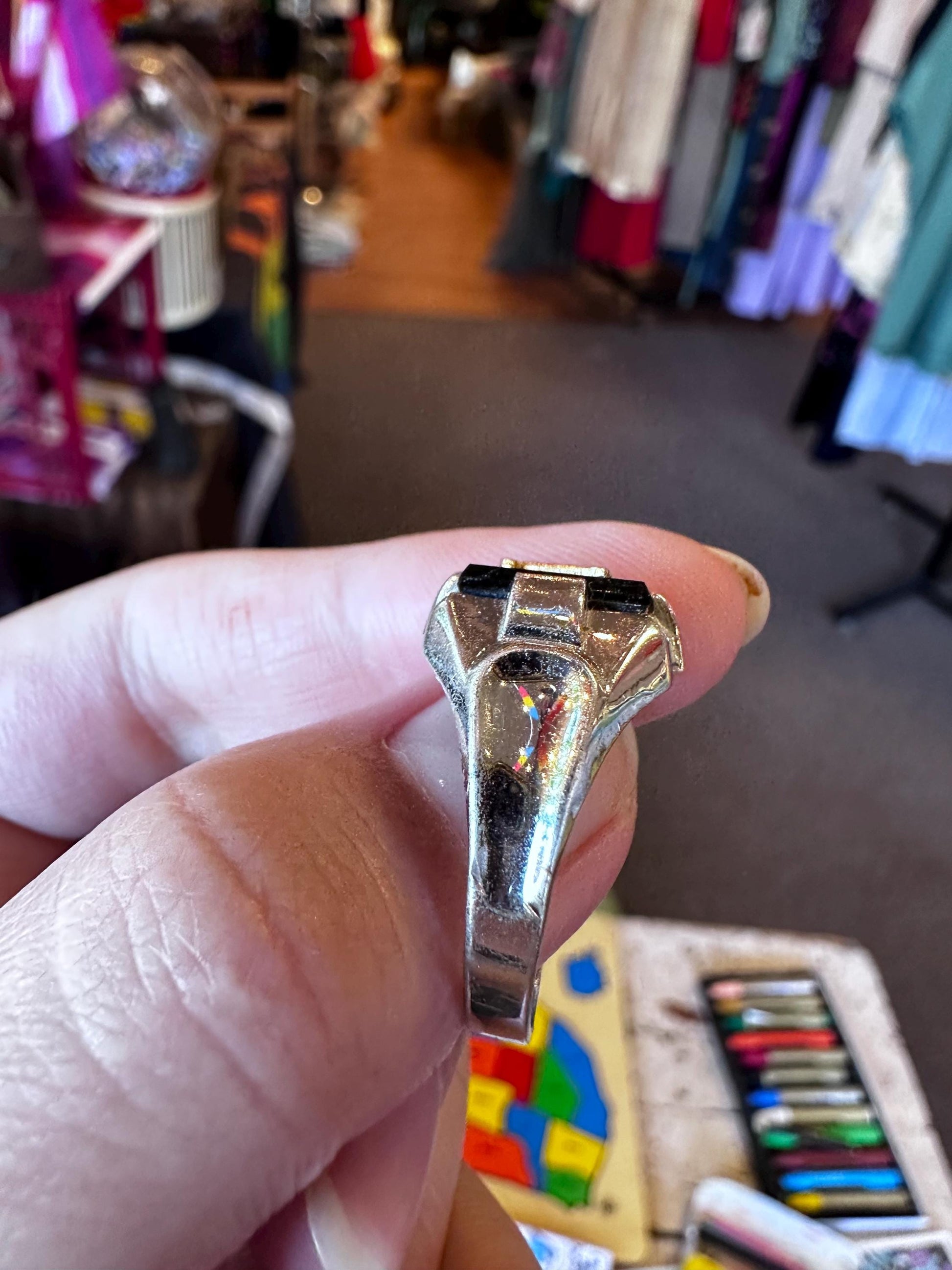 Hand holding a shiny metallic object with a colorful rug and clothing in the background