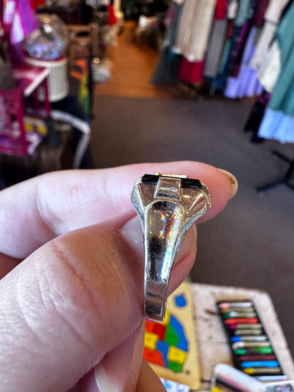 Hand holding a shiny metallic object with a colorful rug and clothing in the background