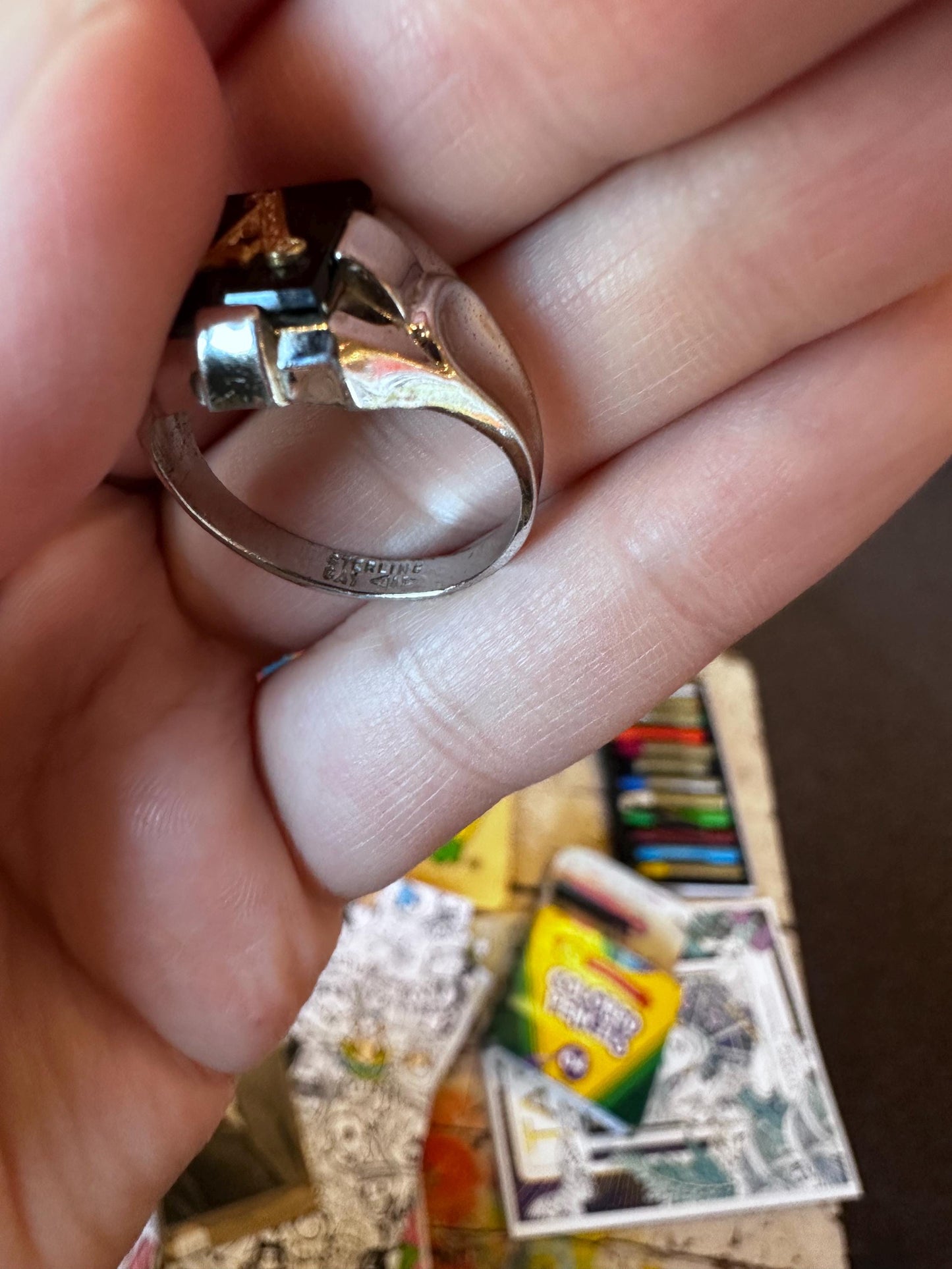 Silver ring held between fingers with a colorful book in the background