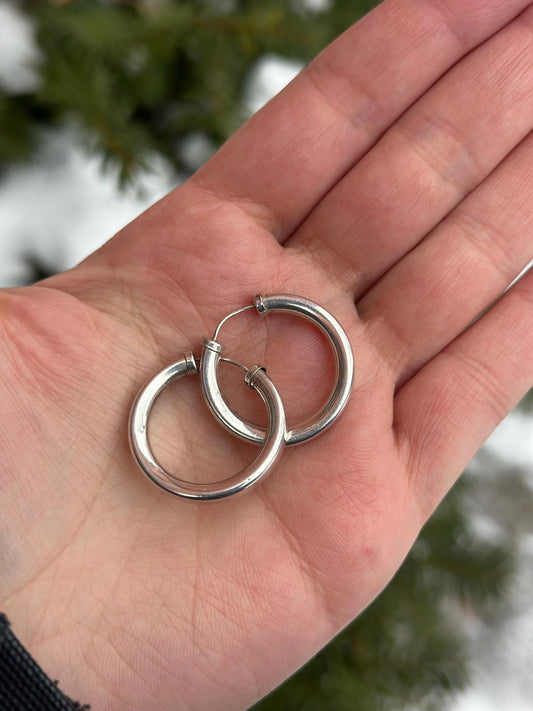 Silver hoop earrings held in a hand with a blurred natural background