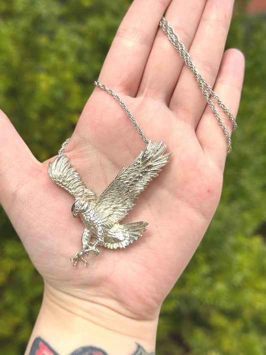 Silver eagle pendant on a chain held in a hand with a blurred green background