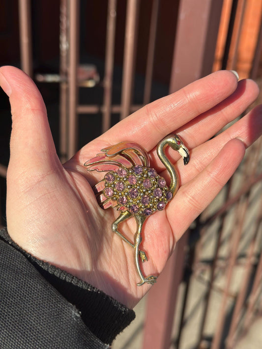 Hand holding a decorative flamingo brooch with gemstones against a blurred background